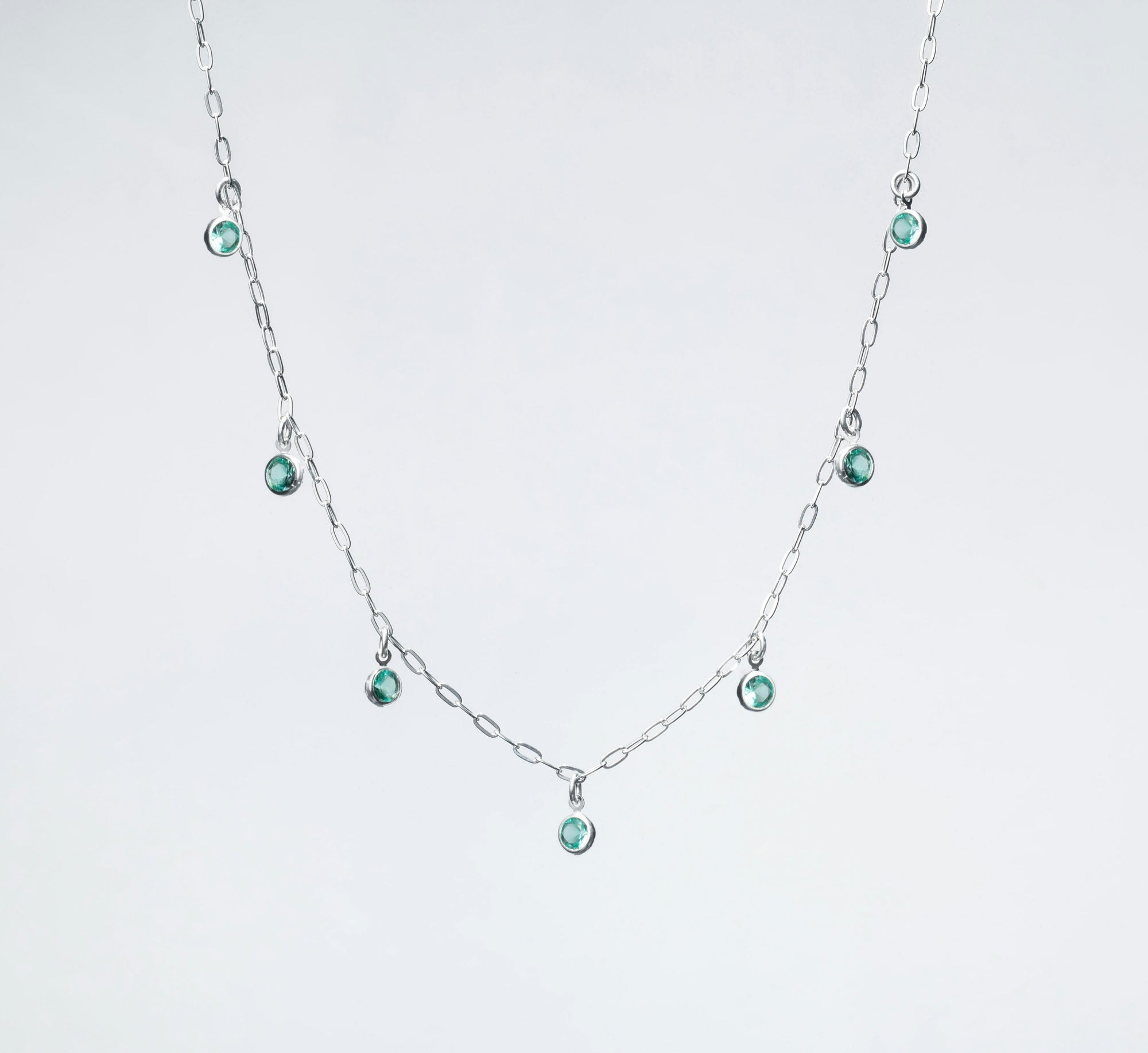 A silver necklace with small green gems