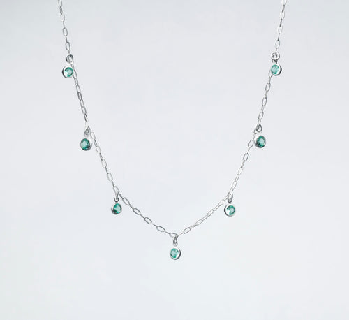 A silver necklace with small green gems